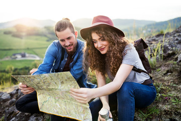 Young tourist couple travellers with backpacks hiking in nature, using map.