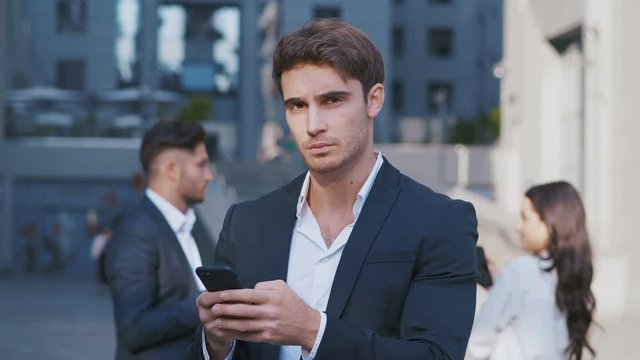 Portrait of busy Business Man using Smartphone and group of business people discussing work in the background. Working in Central Business District. Wearing Classical Suits.