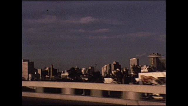 Vintage footage of view from moving car of the New York skyline passing in distance.