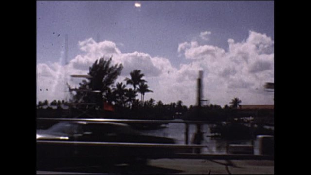 Vintage footage of 1970s USA city driving past classic cars and palm trees.