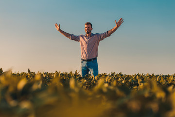 Portrait of farmer standing in soybean field at sunset with his arms outstretched.