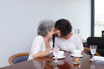 Fototapeta na wymiar Happy mother with adult daughter laughing together. Cheerful senior mother and middle aged daughter sitting together at table with cups and glasses. Togetherness concept