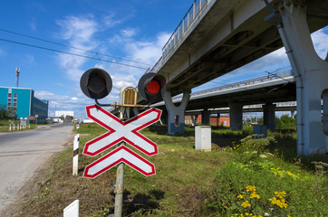 Red traffic light at a railway crossing in an industrial area in the background of a blue sky