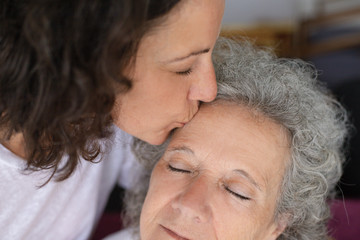 Adult daughter kissing elderly mother. Close-up view of middle aged woman kissing senior mother...