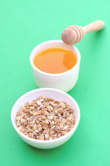 A plate of granola with honey and a spoon on a green background.
