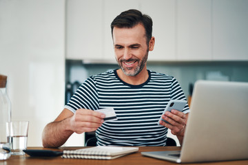 Smiling man shopping online from home with credit card and phone