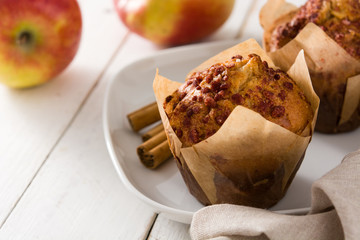 Apples and cinnamon muffins on white wooden table. 