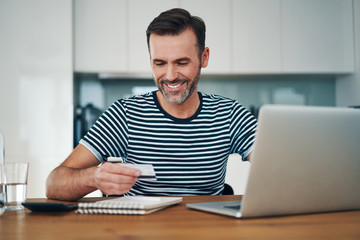 Smiling man using credit card to do online shopping on laptop at home