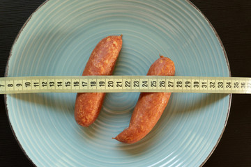 Diet conept - sausages on the plate wrapped with yellow measuring tape