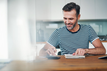 Smiling man using notebook and calculator to manage home budget - Powered by Adobe