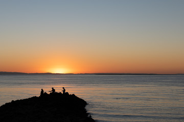 Three men are fishing as the sun sets over the landscape on North Stradbroke Island, Queensland, Australia