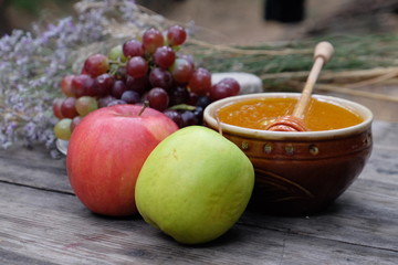 Organic honey in the bowl, wooden honey deeper, apple, grapes, and dry herbs on wooden background, healthy lifestyle, apiculture, healthy products and food, beekeeping, hive honey harvesting