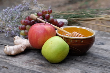 Organic honey in the bowl, wooden honey deeper, apple, ginger, grapes, and dry herbs on wooden background, healthy lifestyle, apiculture, healthy products and food, beekeeping, hive honey harvesting