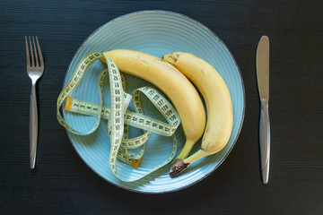 Diet concept - bananas on plate with yellow measuring tape