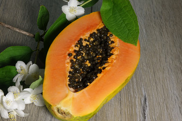 Fresh sliced papaya with seeds inside on a wooden background with jasmine flowers. Half of yellow papaya