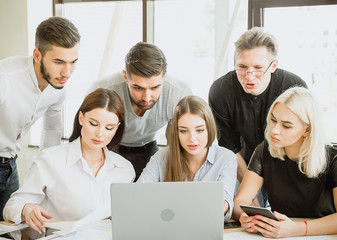 A group of six students are working on a project with a laptop