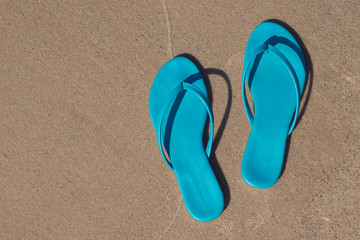 Fototapeta na wymiar Blue beach slippers lie on the sand. Slates on the beach by the sea. Space for text.