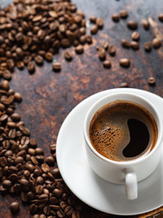 A Cup of espresso on a rusty background with scattered roasted coffee beans . copy space