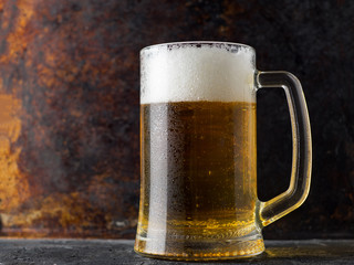 Glass mug of light beer on a dark rusty background