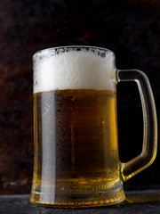 Glass mug of light beer on a dark rusty background
