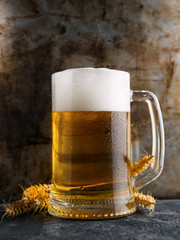 A mug of beer on a rusty background and ears of wheat. Close-up of a pint of beer cold glass
