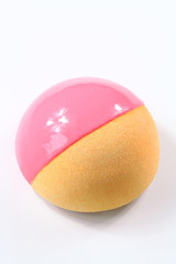 Contemporary Dome Mousse Cake with pink grapefruit, orange and cream cheese mousse, covered with velvet spray and pink mirror glaze, on white background.