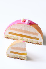 Contemporary Dome Mousse Cake with pink grapefruit, orange and cream cheese mousse, covered with velvet spray and pink mirror glaze, on white background.