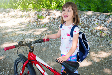 Obraz premium A portrait of a happy child with a backpack and bike on the street.