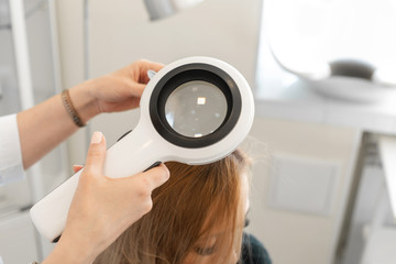Doctor trichologist dermatologist examines the patient's hair and scalp with a dermatoscope