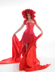 full length portrait of girl wearing long red silk gown and flower headdress. standing pose on white studio background.