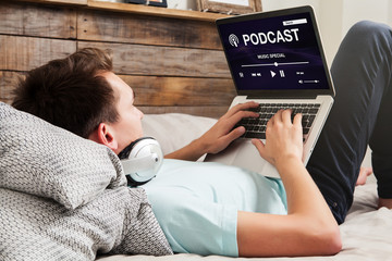 Man listening podcast on the internet with a laptop computer while lying down on the bed.