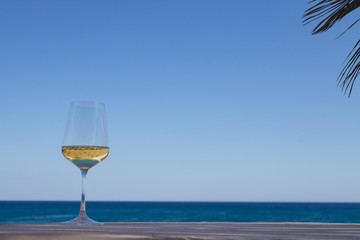 Glass of white wine on the table with shadow from palm and reflection of the beach