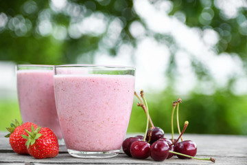A glass of fresh cold smoothie with berries and cherrys on a wooden table, summer set, outdoor greed blured background,boke.