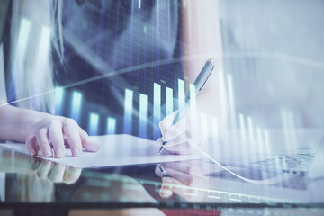 A woman hands writing information about stock market in notepad. Forex chart holograms in front....