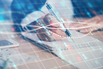 A woman hands writing information about stock market in notepad. Forex chart holograms in front....