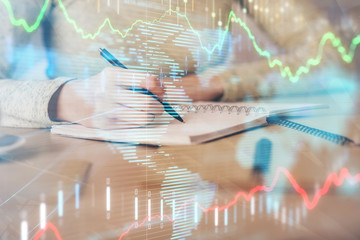 Hands writing information about stock market in notepad. Forex chart holograms in front. Concept of research. Multi exposure