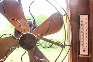 Antique Fan in a window next to a thermometer reading over 100 degrees on a hot summer day 