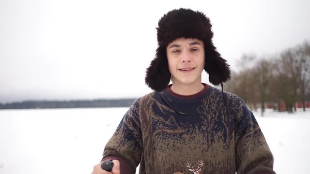 A man in a hat with earflaps freezes in the street. A handsome guy in a sweater is standing on a winter street.A handsome young guy warms his hands in winter.