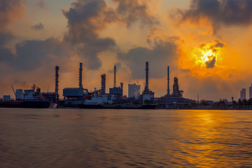 Obraz premium The sun shines through the dark clouds to the oil refinery, Beautiful factory with morning sky-Image