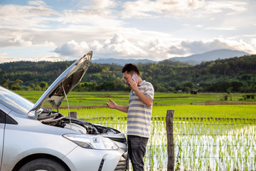 Broken car while traveling far to travel,asian male calling assistance on the phone to help with the breakdown of the car on street,man having problem near a broken car at the side of road