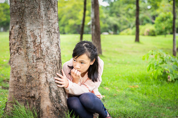 Asian child girl biting fingernails,person scared suffering paranoid,worried concerned sitting at outdoor park,increasing fear anxiety,stressed and nervous insecure,hallucinations,depression concept