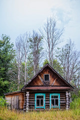 Old wooden house on the background of bare trees and cloudy sky