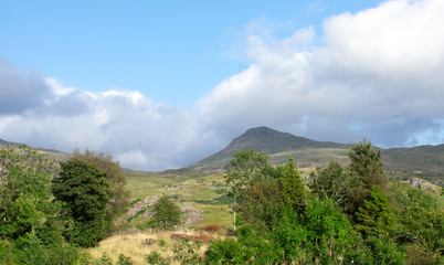 Wales, the Snowdonia national park. The rolling hills before the high peaks. A summers day. Fair weather cloud and blue skies. Shadows on the rugged green hill sides. Open air, health and nature.