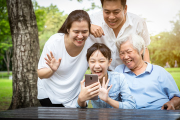 Communication technology,happy asian family laughing with smartphone,daughter,father,mother,grandmother talking to each other through a video call on a smartphone,parents with child girl enjoying park