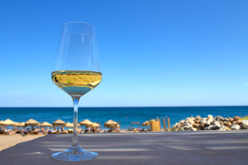 Glass of white wine on the table with shadow and reflection of the beach inside, sky and sea on the background.