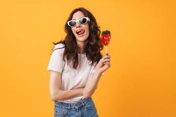 Happy cute young woman posing isolated over yellow wall background holding candy lollipop.