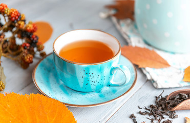 composition still life of a mug with hot leaf tea with berries and autumn leaves on a wooden surface