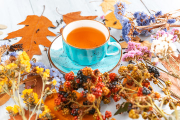 composition still life of a mug with hot leaf tea with berries and autumn leaves on a wooden surface