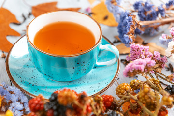 composition still life of a mug with hot leaf tea with berries and autumn leaves on a wooden surface