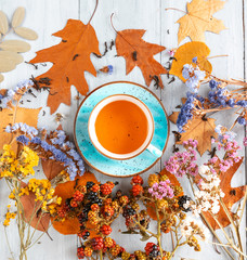 composition still life of a mug with hot leaf tea with berries and autumn leaves on a wooden surface